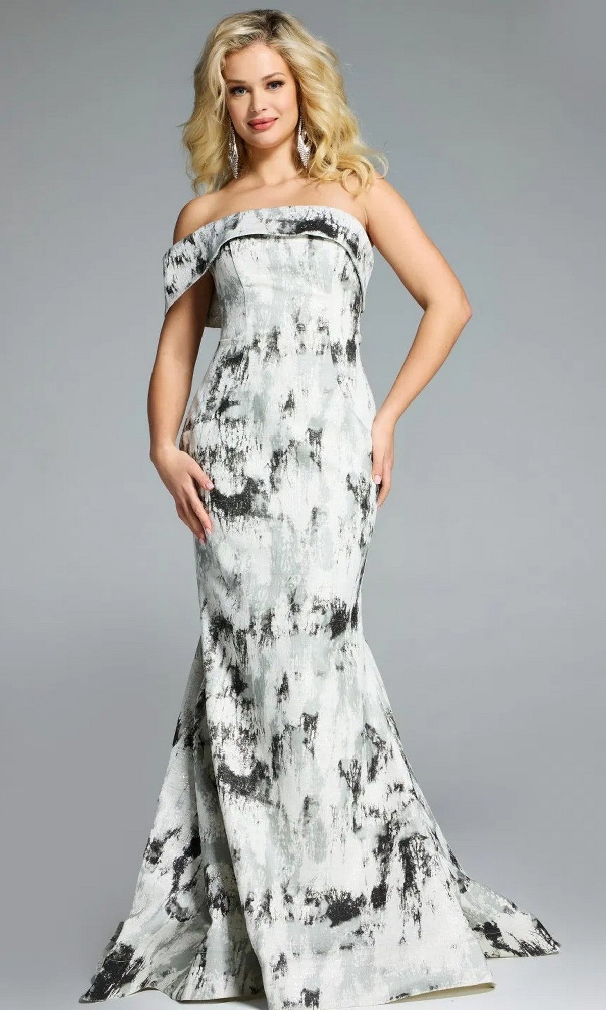 A woman stands against a plain background wearing the Jovani 43977 long prom dress—an off-the-shoulder, floor-length gown with a black and white abstract print and an elegant mermaid silhouette.